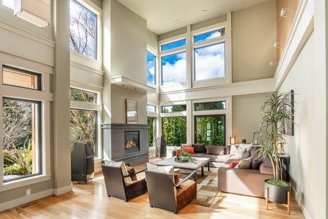 Sunlit two-story living room with floor-to-ceiling windows and a fireplace