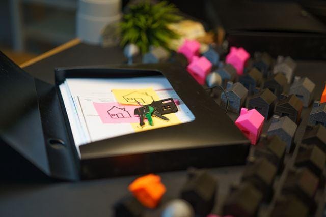House keys and a sticky note resting on a folder beside rows of small model houses