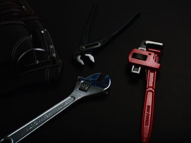Adjustable wrench, pipe wrench, and pliers laid out on a dark surface