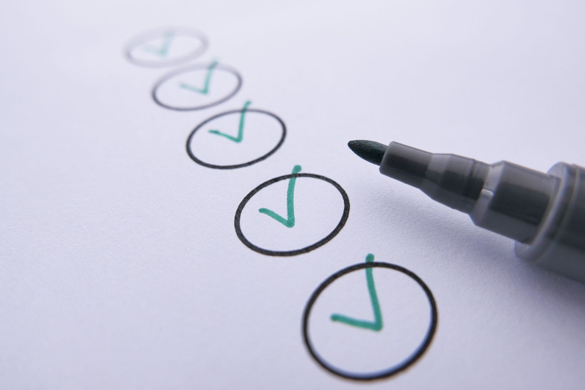 Green checkmarks inside circles on a printed page, with a felt marker resting beside the bottom mark
