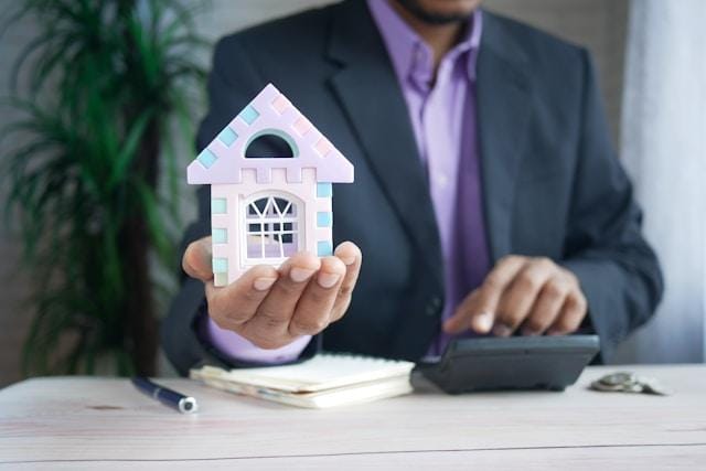 Property manager holding a small model house while working a calculator