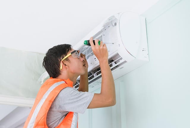 Technician in a safety vest servicing a wall-mounted air conditioning unit